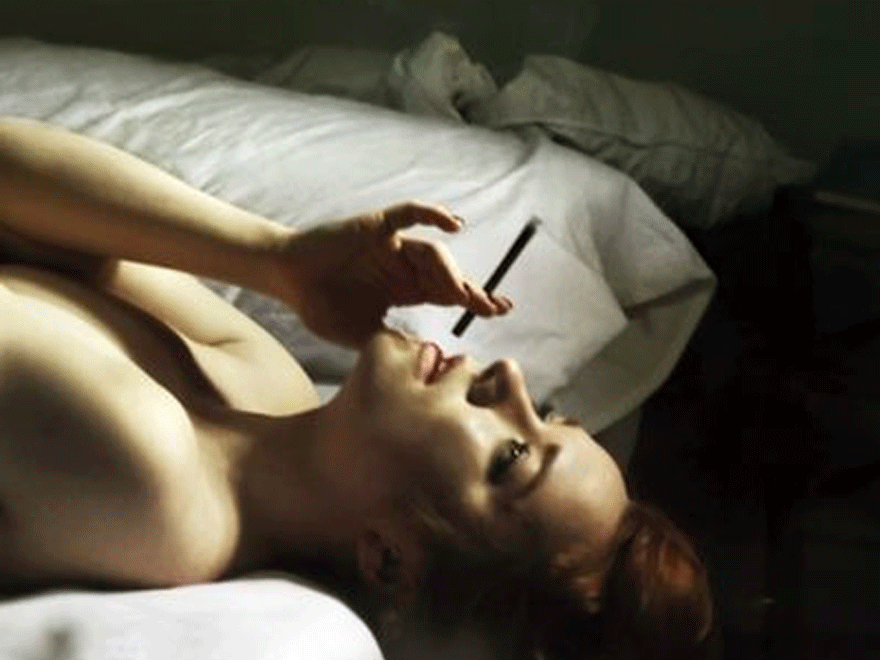 Imagen de una mujer fumando tumbada en la cama